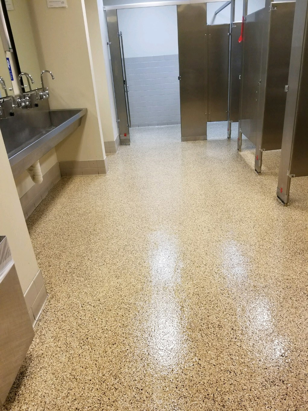 Tan and brown flake epoxy floor coating in a commercial restroom with stainless steel stalls