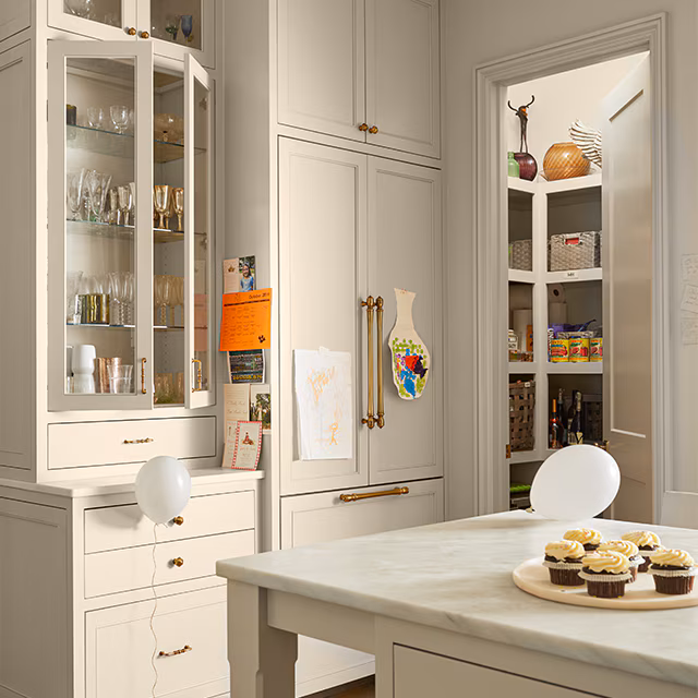 Soft beige painted kitchen cabinets with brass hardware and a glass-front display cabinet